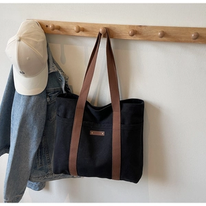 Vue détaillée d'un sac cabas en toile noire avec anses marron suspendu dans une maison