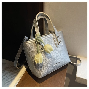 Detail of silver textured leather bucket bag with a tulip charm on a wooden table