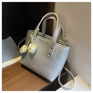 Detail of silver bucket bag with lychee texture and a floral tulip charm on a wooden table