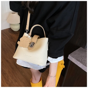 Detail of cream bucket bag with lychee texture, metal lock and cute dog charm accessory