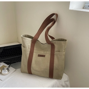 Detail of khaki canvas tote bag with brown straps and side pockets on office desk