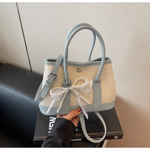 Close-up of pearl lace bow and light blue leather texture on a two-tone bucket bag