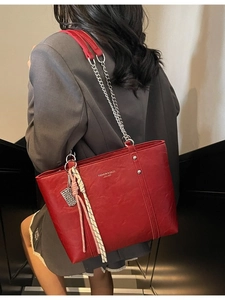 Fashionable red faux leather tote bag with chain strap and pendant shown on model