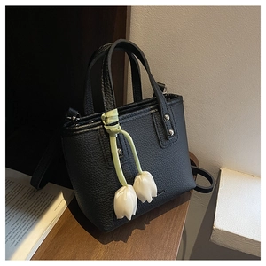 Detail of black litchi leather bucket bag with a white tulip pendant on a wooden shelf
