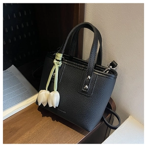 Detail of black lychee grain bucket bag featuring a white tulip charm and silver rivets