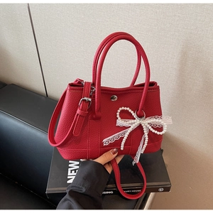 Close-up of red lychee textured bucket bag featuring a pearl and lace bow decoration