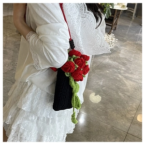 Dettaglio borsa a secchiello in maglia fatta a mano con rose rosse e foglie verdi