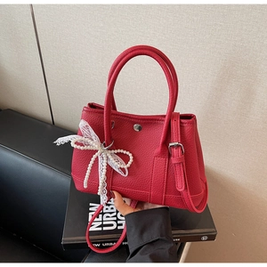 Detail of red lychee leather bucket bag featuring pearl and lace bowknot accessory
