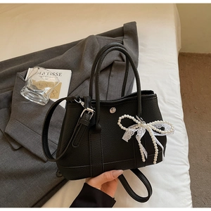Detail of black pebbled leather bucket bag with lace bow and pearl decoration