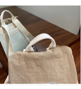 Dettaglio della borsa a secchiello beige pieghettata con manici intrecciati e cuciture