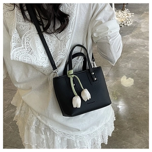 Detail of black lychee texture bucket bag with white tulip charm on model