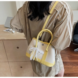 Chic cream bucket bag with yellow trim and pearl lace bow charm shown as crossbody