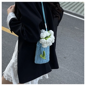 Dettaglio borsa a secchiello blu all'uncinetto con fiori 3D bianchi e foglie verdi