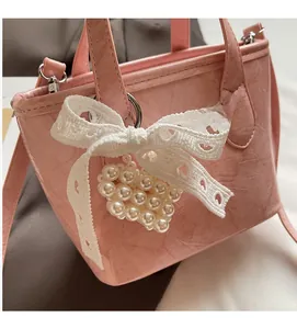 Dettaglio borsa a secchiello rosa con fiocco di pizzo e pendente a cuore di perle su pelle