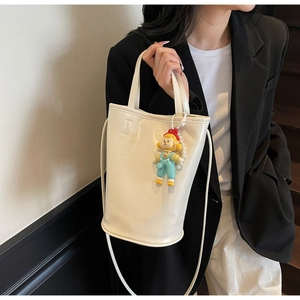Détail d'un sac seau blanc avec texture en cuir brillant et un joli pendentif cartoon