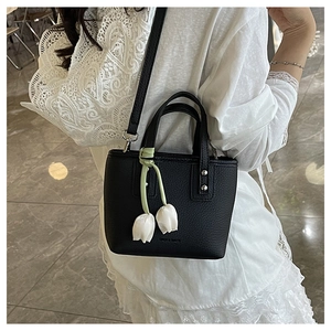 Detail of black leather bucket bag with a white tulip charm and a cylindrical handle