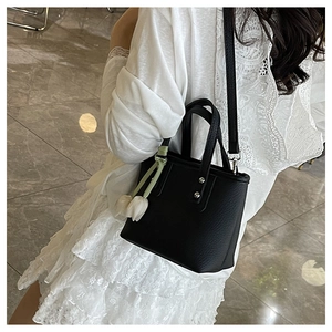 Detail of black pebbled leather bucket bag with white tulip charm and shoulder strap