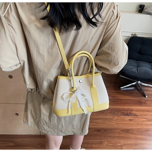 Close-up of cream and yellow bucket bag with pearl lace bow detail on wood floor