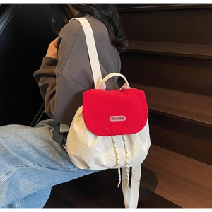 Detail view of mini canvas drawstring backpack with red flap and cream body worn by a model