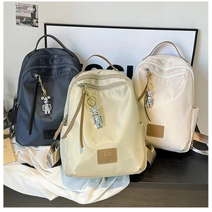 Three minimalist waterproof nylon backpacks in grey, gold, and white with bear charms