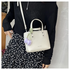 Detail of a beige lychee pattern bucket bag with a purple tulip pendant and strap