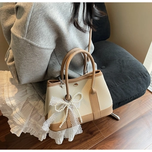 Detail of cream and brown bucket bag with pearl lace bow charm in home setting