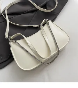 Detail of white half-moon bag with silver metal chain and smooth faux leather texture