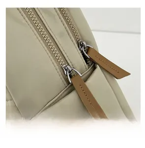 Detail of light beige nylon backpack featuring dual zippers with brown leather pull tabs