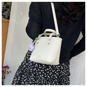Detail of cream white bucket bag with silver studs and a purple tulip charm accessory