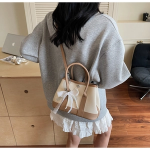 Detail of a mini beige bucket bag with lace bow and pearl chain on a stylish model