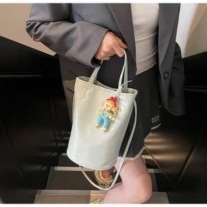 Detail van lichtgroene emmer-tas van rimpelleer met schattige bedel en smalle schouderriem
