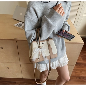 Close-up of beige and brown bucket bag with lace bow and pearl charm detail