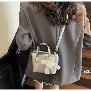 Borsa a secchiello argento con fiocco in pizzo e ciondolo a cuore di perle su blazer