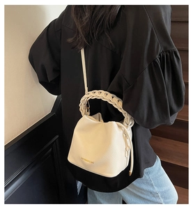 Close-up of beige lychee leather bucket bag with braided handle worn by model