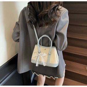 Detail of cross-body bucket bag with pearl lace bow and blue trim on beige leather