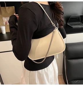 Detail of beige crescent underarm bag with silver chain strap shown on a model's shoulder