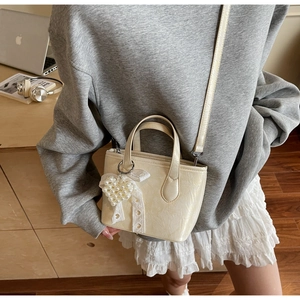Dettaglio della mini borsa tote bianco crema con ciondolo a cuore e fiocco in pizzo