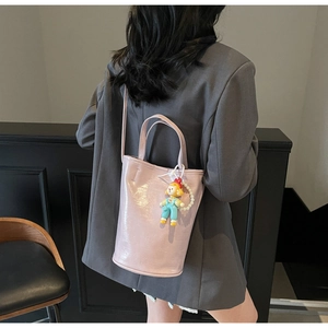 Détail du sac seau en cuir verni rose clair avec charm poupée mignon et longue bandoulière