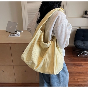 Detailed view of yellow pleated fabric tote bag with a wide strap on person