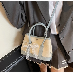 Detail of small bucket bag in beige lychee leather with blue trim and pearl bow charm