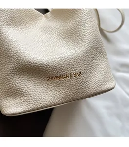 Close-up of beige leather bucket bag featuring luxury lychee texture and gold logo detail