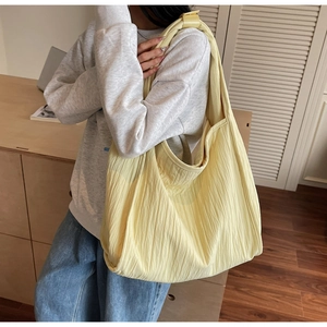 Detail of pale yellow pleated hobo bag showing textured nylon fabric and wide strap
