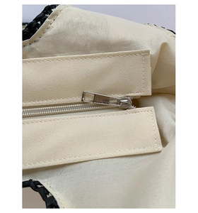 Close-up of metal zipper and beige lining inside the black woven straw tote bag