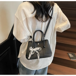 Detail of black leather bucket bag with white lace and pearl bow charm on model
