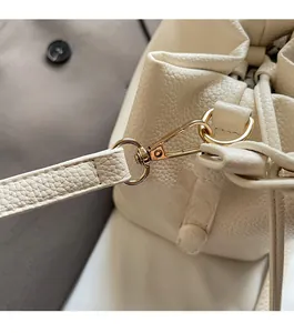 Close-up of golden metal hooks and buckles on a cream-white lychee pattern leather bag