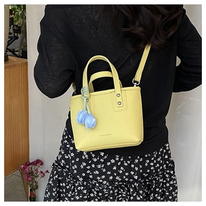 Yellow bucket bag with blue tulip charm shown on shoulder for proportion and fit