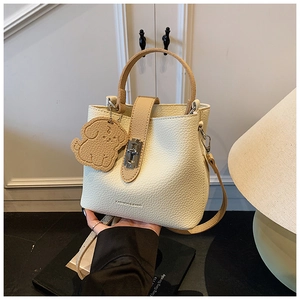 Close-up of creamy white lychee textured bucket bag with puppy charm and metal lock