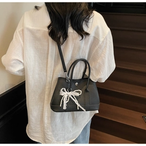 Detail of black pebbled leather bucket bag with white lace bow and pearl charm ornament
