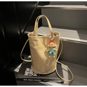 Détail d'un sac seau en cuir crème avec un charm de dessin animé et une bandoulière