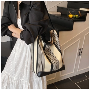 Close-up of a large striped tote bag with leather trim held by a model in a stylish interior